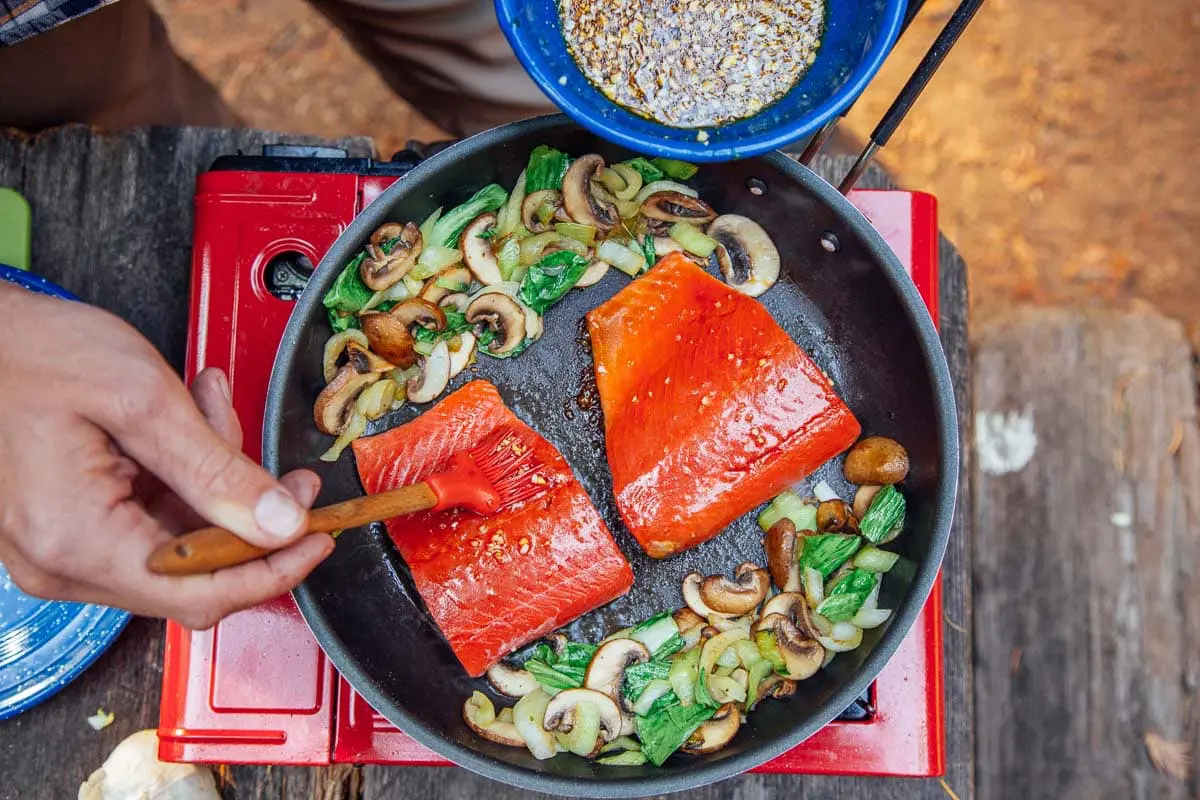 Basting honey-soy glaze on to two salmon fillets in a skillet.