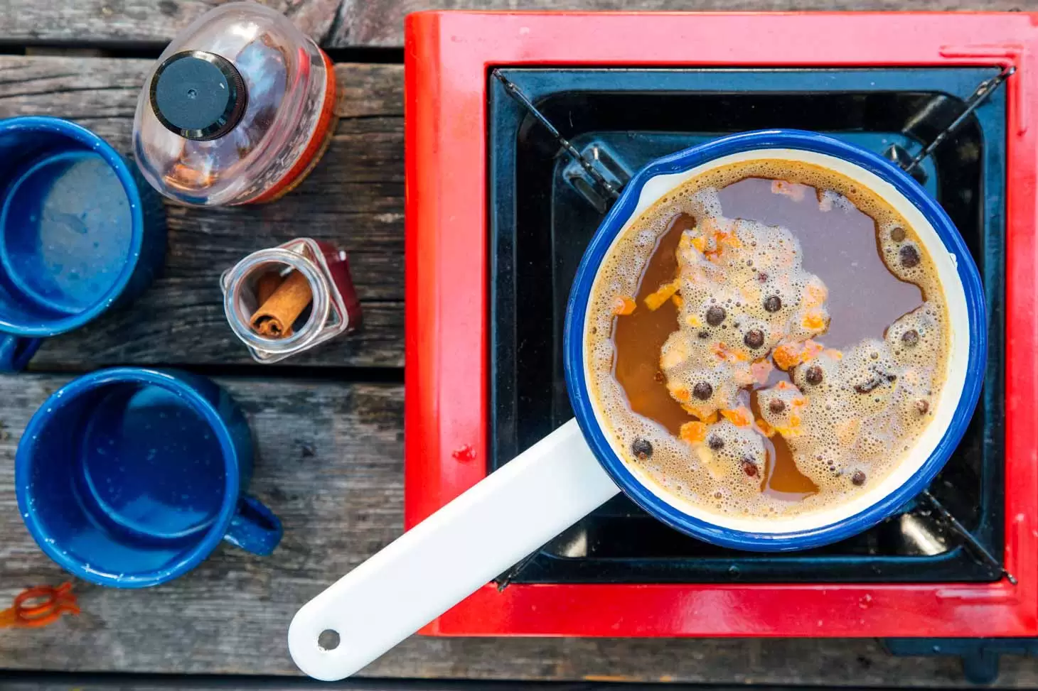 Spiked apple cider with mulling spices in a small white enamel pot on a camping stove.