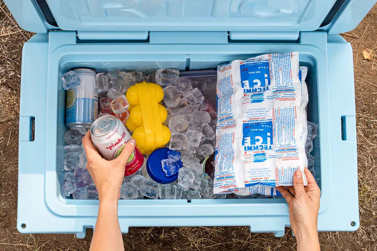 Hands reaching into a blue cooler full of ice to pick up a drink can