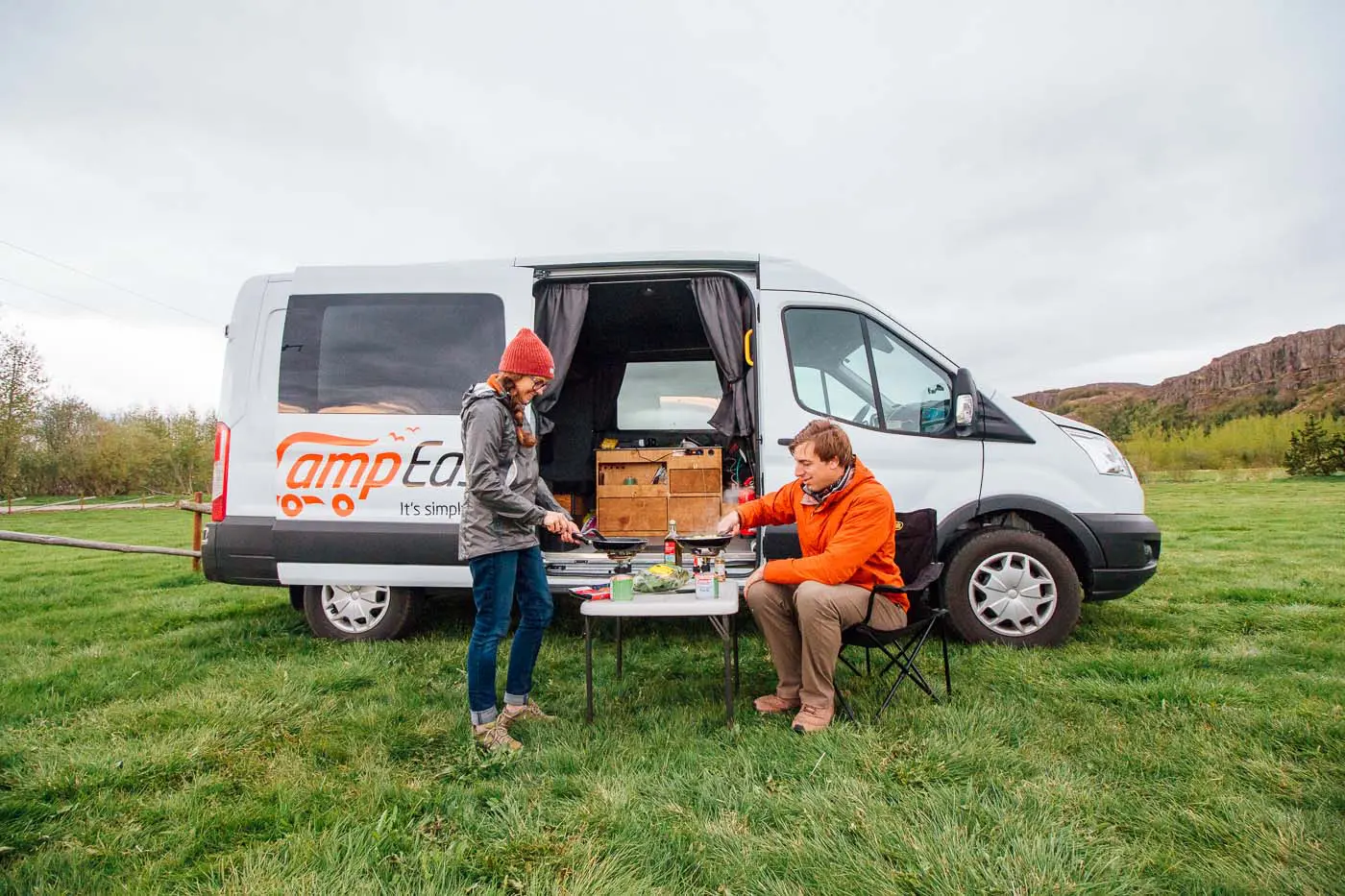 A couple cooking on a small table in front of a Camp Easy camper van in Iceland