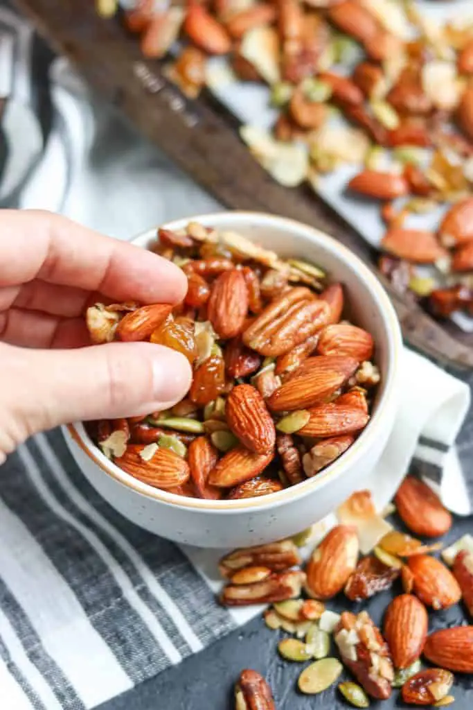 A hand scooping trail mix from a while bowl