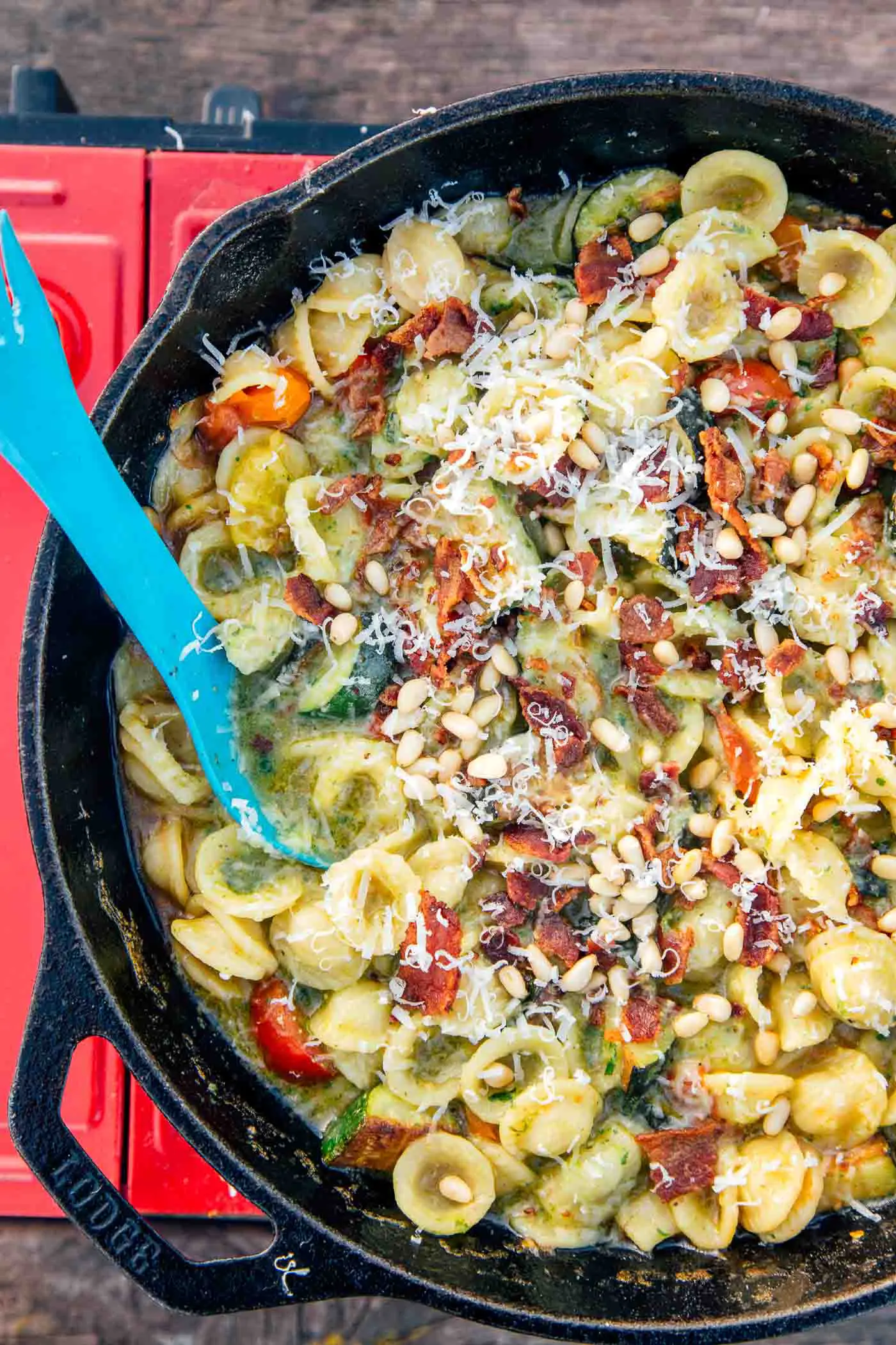 Overhead view of pasta in a pesto sauce in a cast iron skillet on a camping stove.