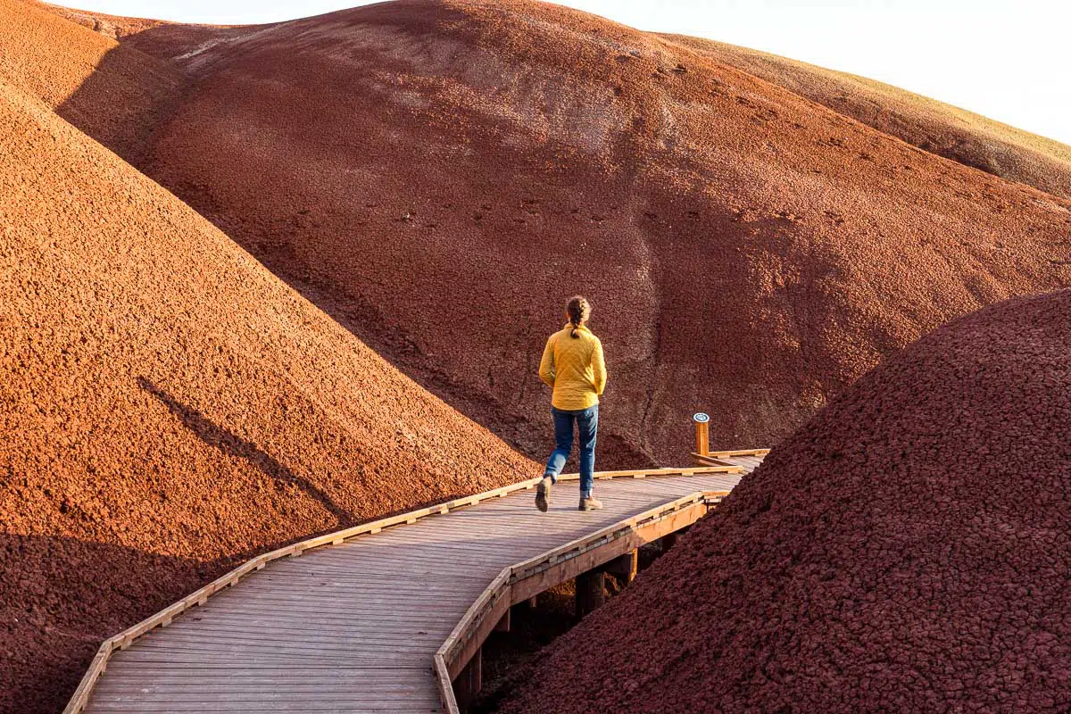 Megan walks along a wooden boardwalk that curves through red hills