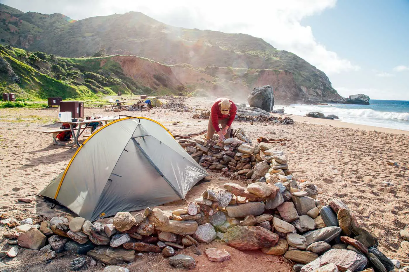 Man creating a wall of rocks around a tent.