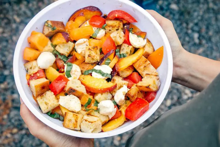 A while bowl of panzanella with torn bread, sliced peaches, tomatoes and cheese