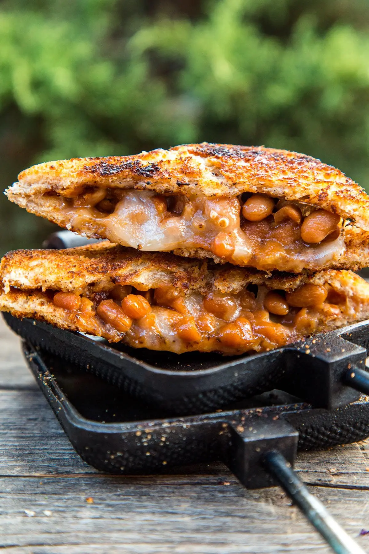 A sandwich filled with beans and cheese cut diagonally in half, resting on an open pie iron