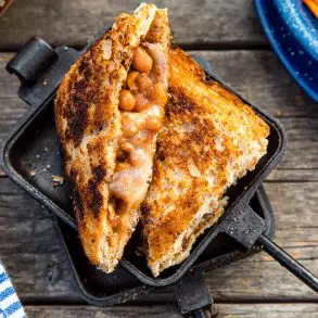 A sandwich filled with beans and cheese cut diagonally in half, resting on a open pie iron