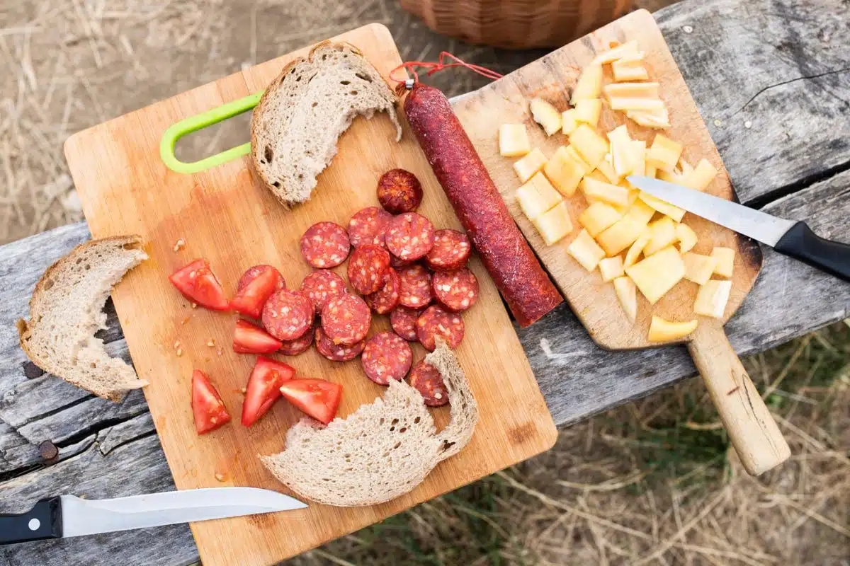 Sliced salami, bread, and cheese on wooden cutting boards.