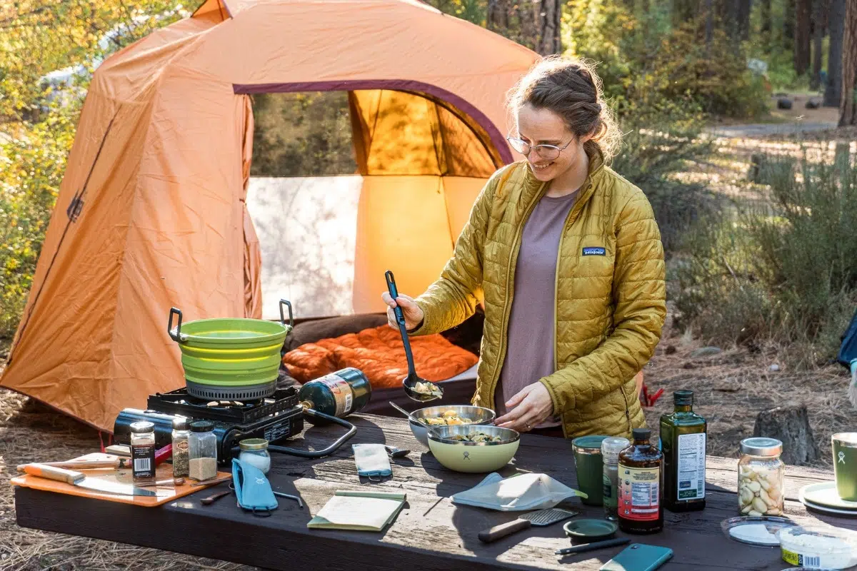 Megan ladling tortellini soup into bowls. A camp scene is in the background