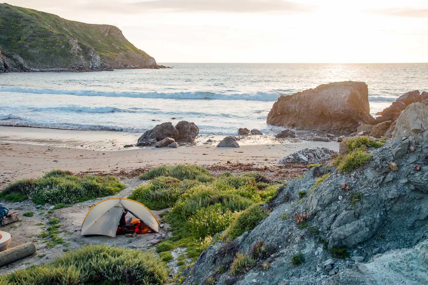 A tent set up on the beach overlooking the ocean at sunset.