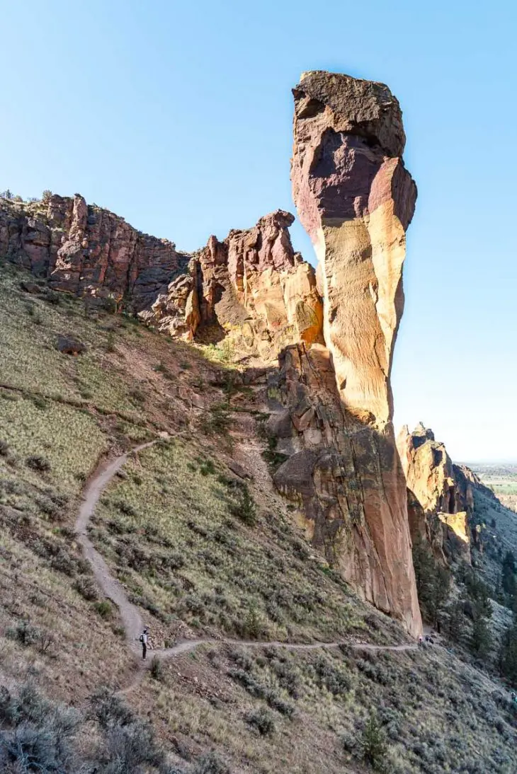 Megan stands on a steep hiking trail and looks up at a rock formation.