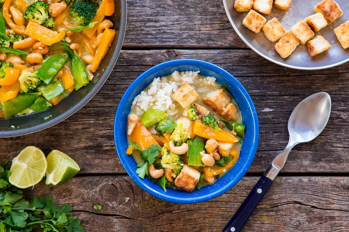 A blue bowl filled with Thai green curry on a wooden camping table