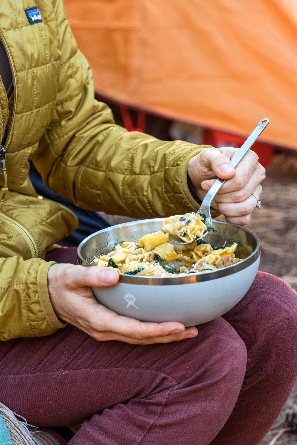 Megan holding a bowl of tortellini soup balanced on her knees