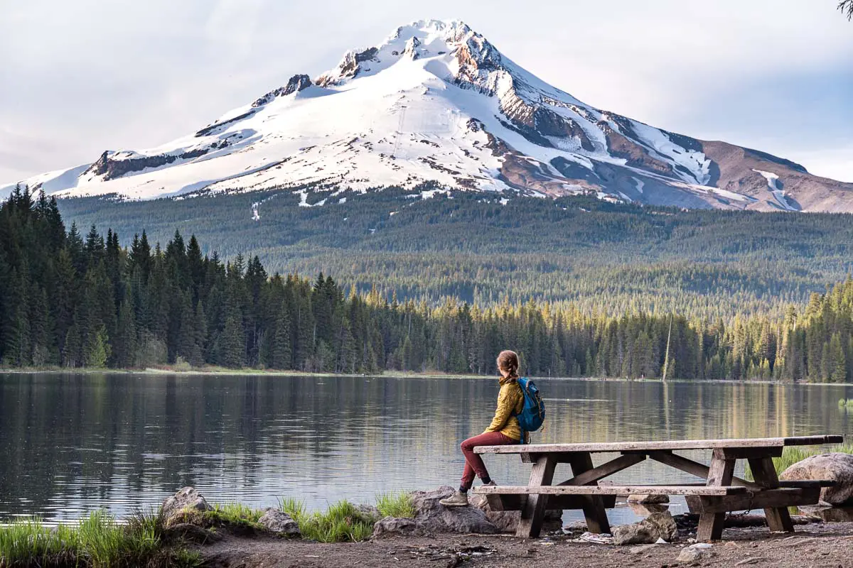 Megan is sitting on a picnic table on the shores of Trillium Lake. Her head is turned and she is looking at Mt. Hood.