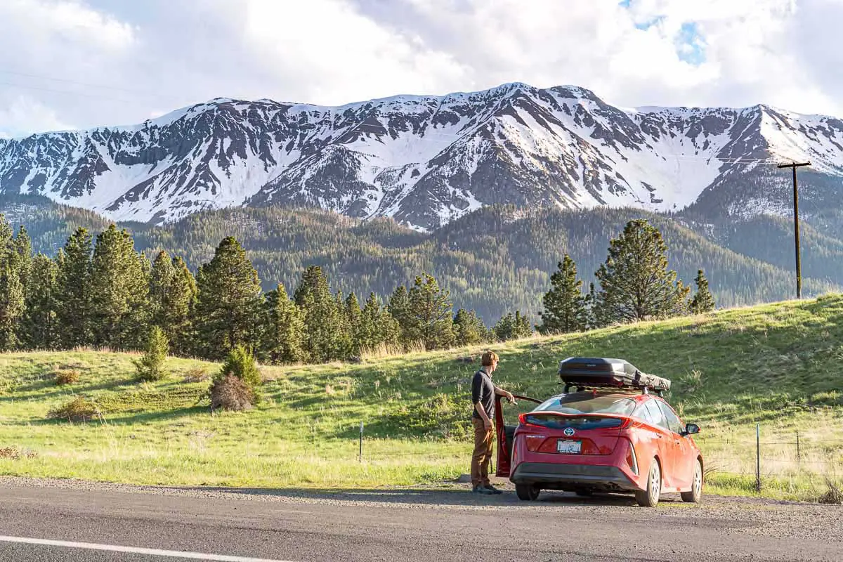 Michael standing next to a red Prius Prime with the Wallowa Mountains in the distance.