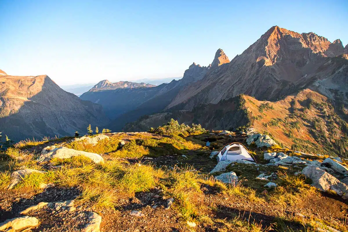 A tent set up in a clearing on a mountain top.