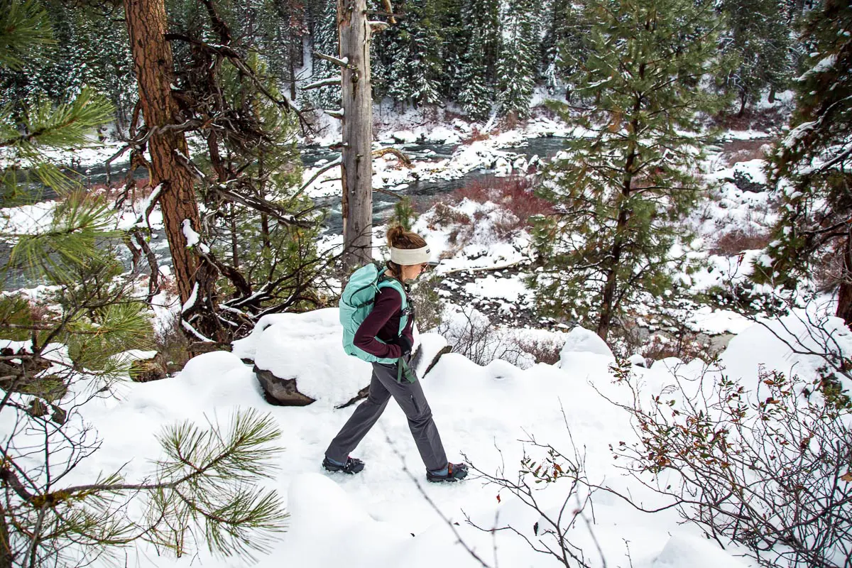 Megan hiking on a snowy trail. She is wearing a wool baselayer top and winter hiking pants.