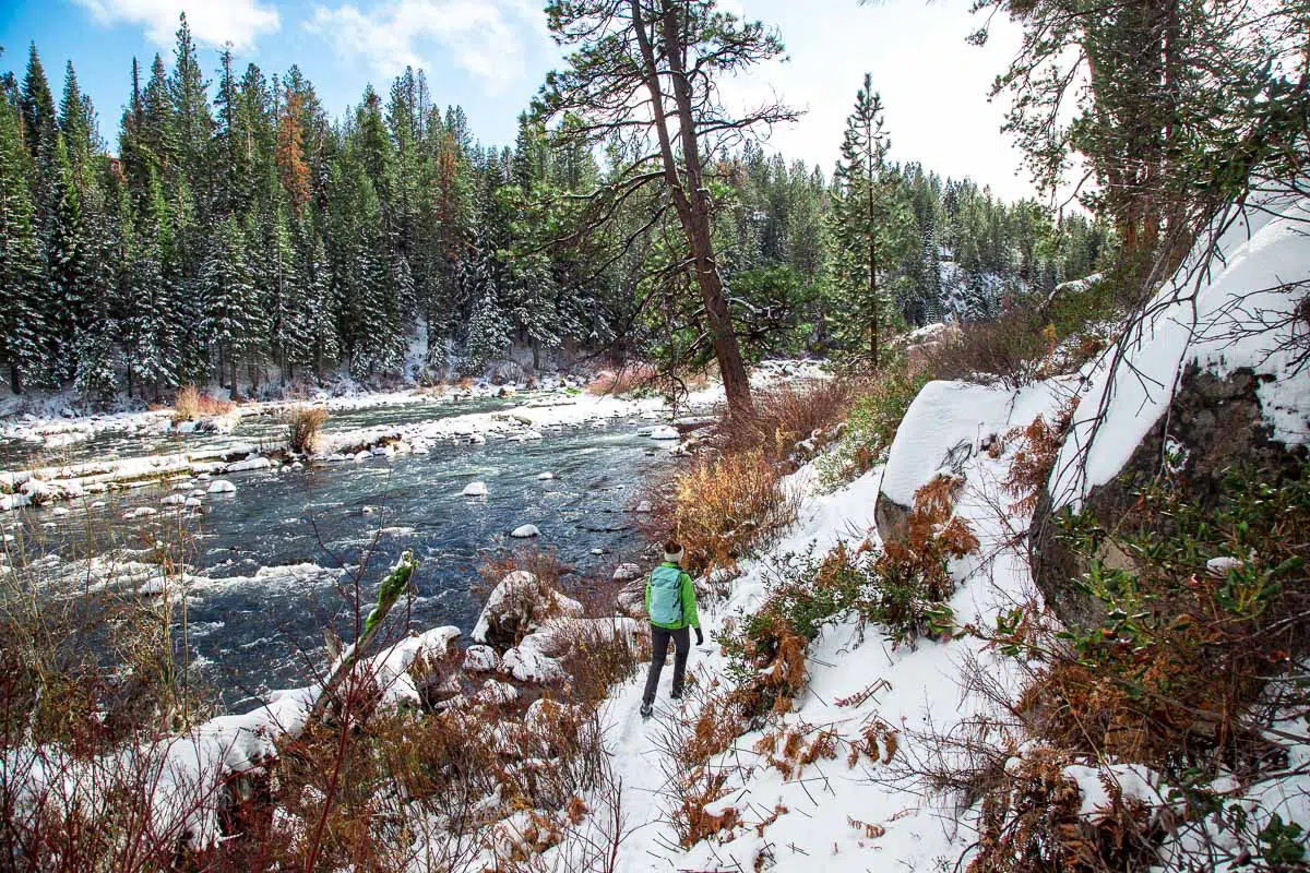 A woman hiking in the snow on a riverbank